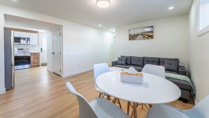 Un salon moderne avec une table à manger ronde, un canapé gris et une cuisine en arrière-plan.