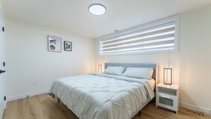 Une chambre à coucher comprenant un lit, des tables de chevet, une fenêtre avec des stores et un luminaire au plafond.