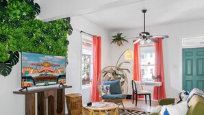Een woonkamer met een televisie waarop een stadsgezicht te zien is, een ronde tafel, een groene bank en een plafondventilator.