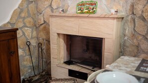 Una chimenea de piedra con repisa, un aparador de madera y una mesa de comedor con platos.