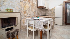 Una cocina con paredes de piedra, chimenea, mesa de comedor con sillas y un refrigerador.
