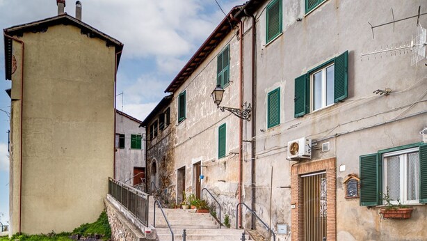 Una calle estrecha con un edificio que presenta una escalera, una puerta y una ventana con contraventanas verdes.