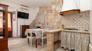 Una cocina con pared de piedra, una mesa de comedor con sillas, un televisor fijado a la pared y una estufa empotrada.
