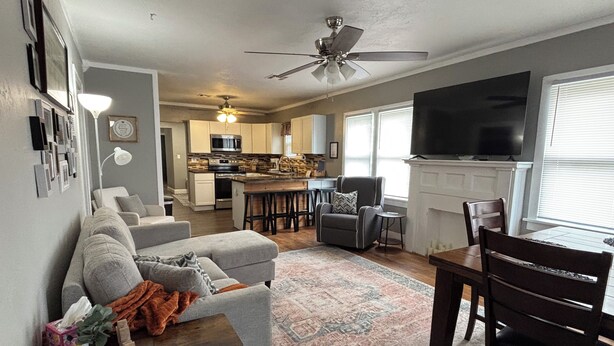 A living room with a grey sofa, a coffee table, and a TV. There is a kitchen in the background with a microwave and cabinets. - Comfortable and Spacious Home close to OSU Campus (Stillwater)