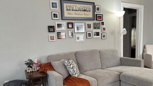A living room with a grey sofa, a small wooden side table, and a wall decorated with framed pictures. - Comfortable and Spacious Home close to OSU Campus (Stillwater)