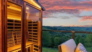 Una sauna de madera con puertas de vidrio, un banco y vista a un paisaje boscoso.