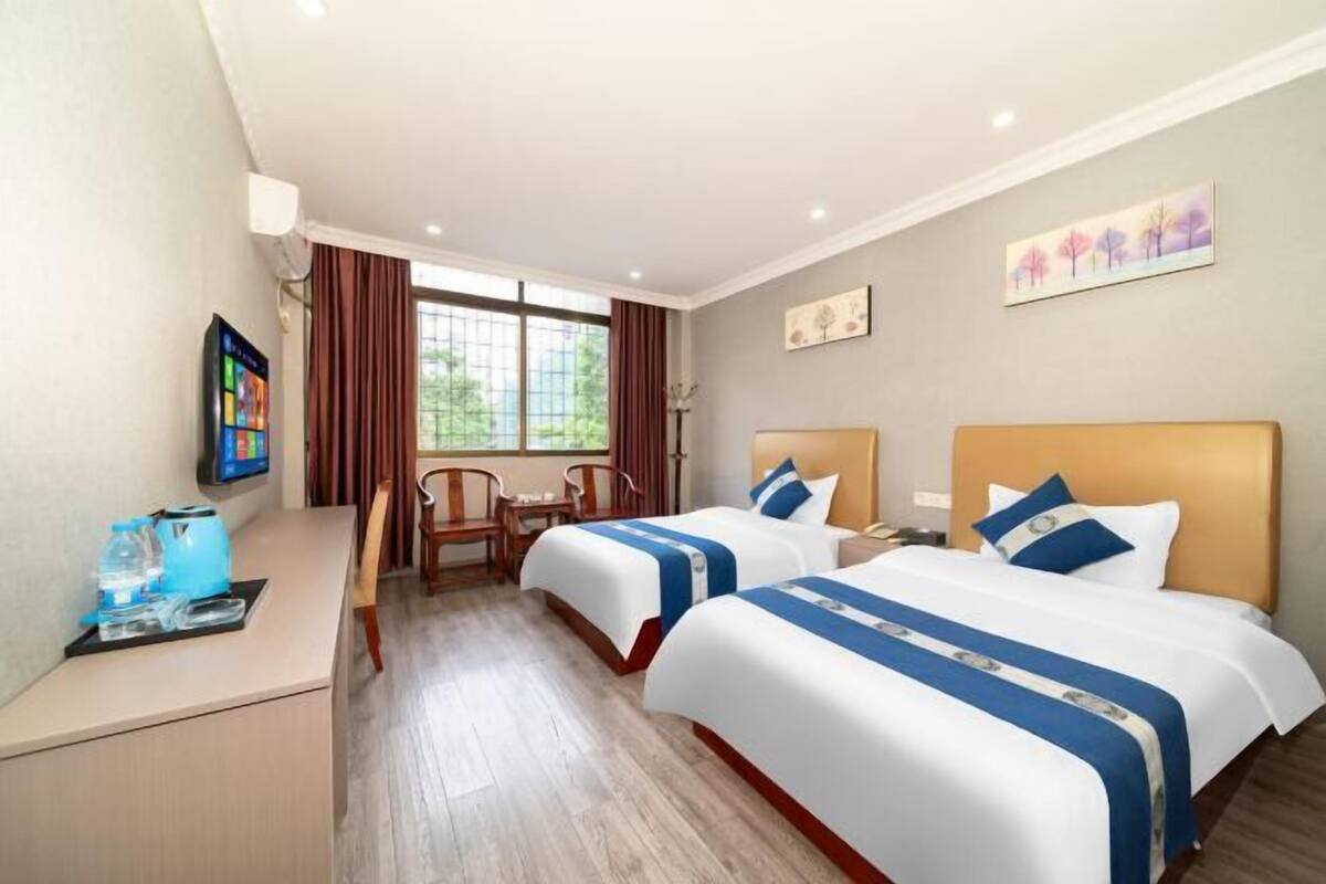 A hotel room with two beds, a desk, a chair, a TV, and a window with curtains.