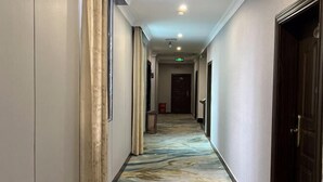 A hotel hallway with a patterned carpet, a door on the right, and a light fixture on the ceiling.