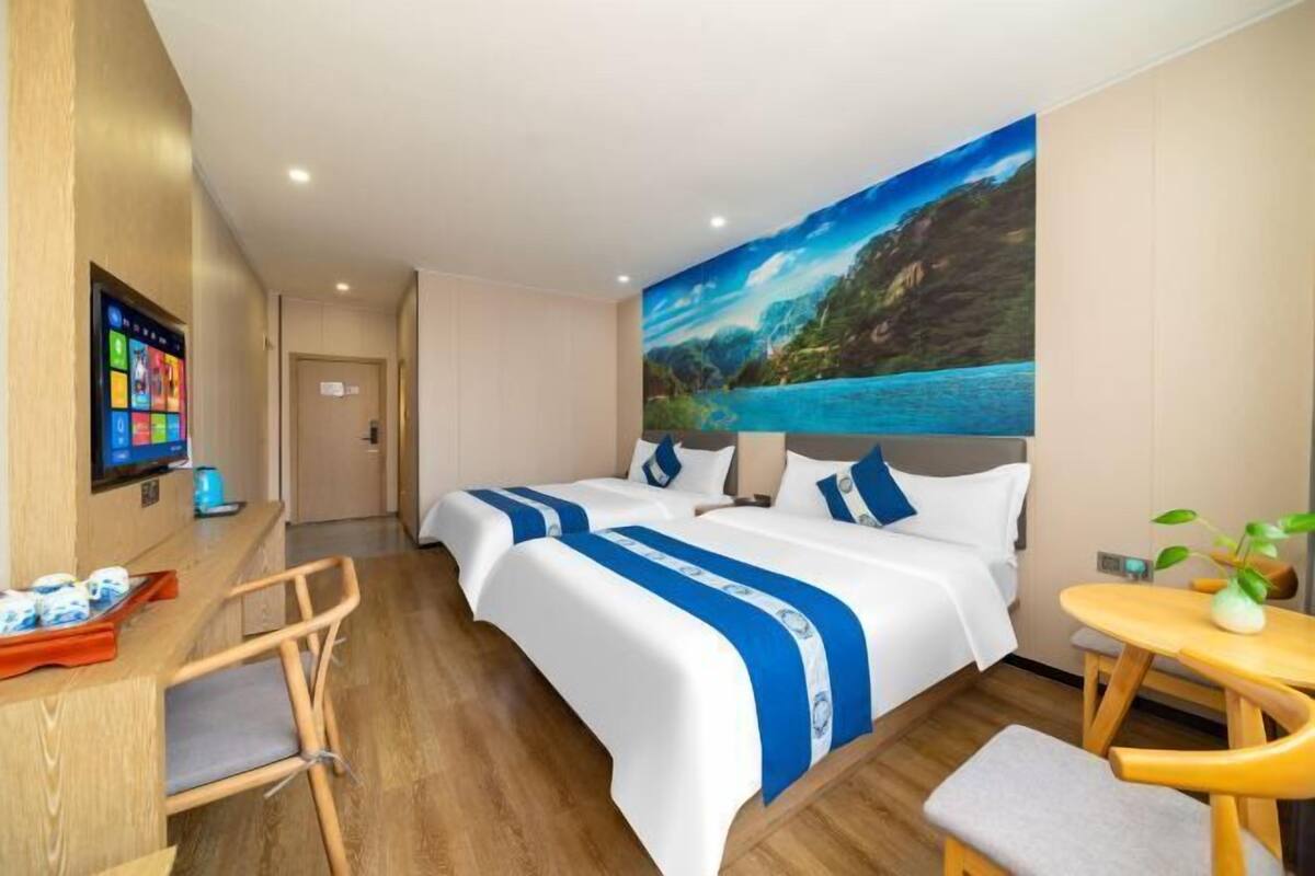 A hotel room with two beds, a desk with a computer, a small table, and a painting of a landscape on the wall.