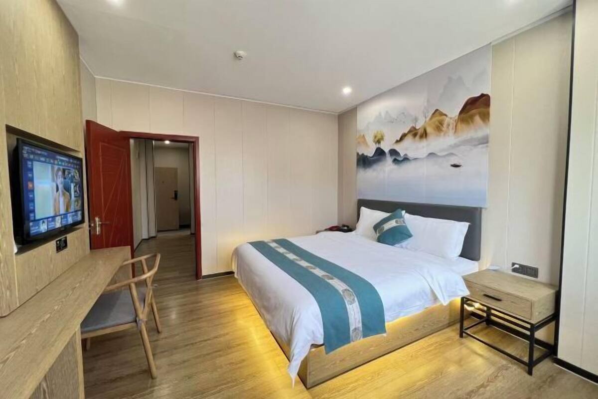 A hotel room with a bed, a desk with a chair, a TV, and a painting on the wall.