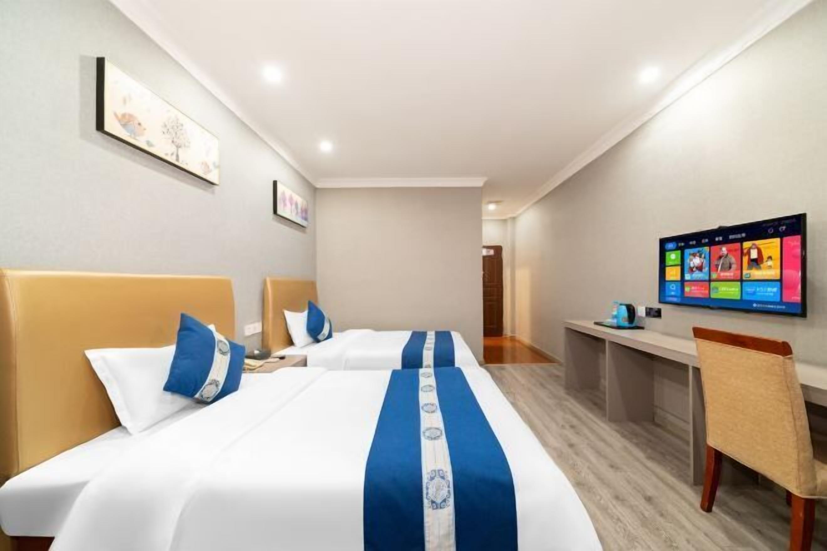 Habitación de hotel con dos camas, un escritorio y televisión en la pared.