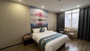 A hotel room with a bed, a nightstand, a small table, and a chair.