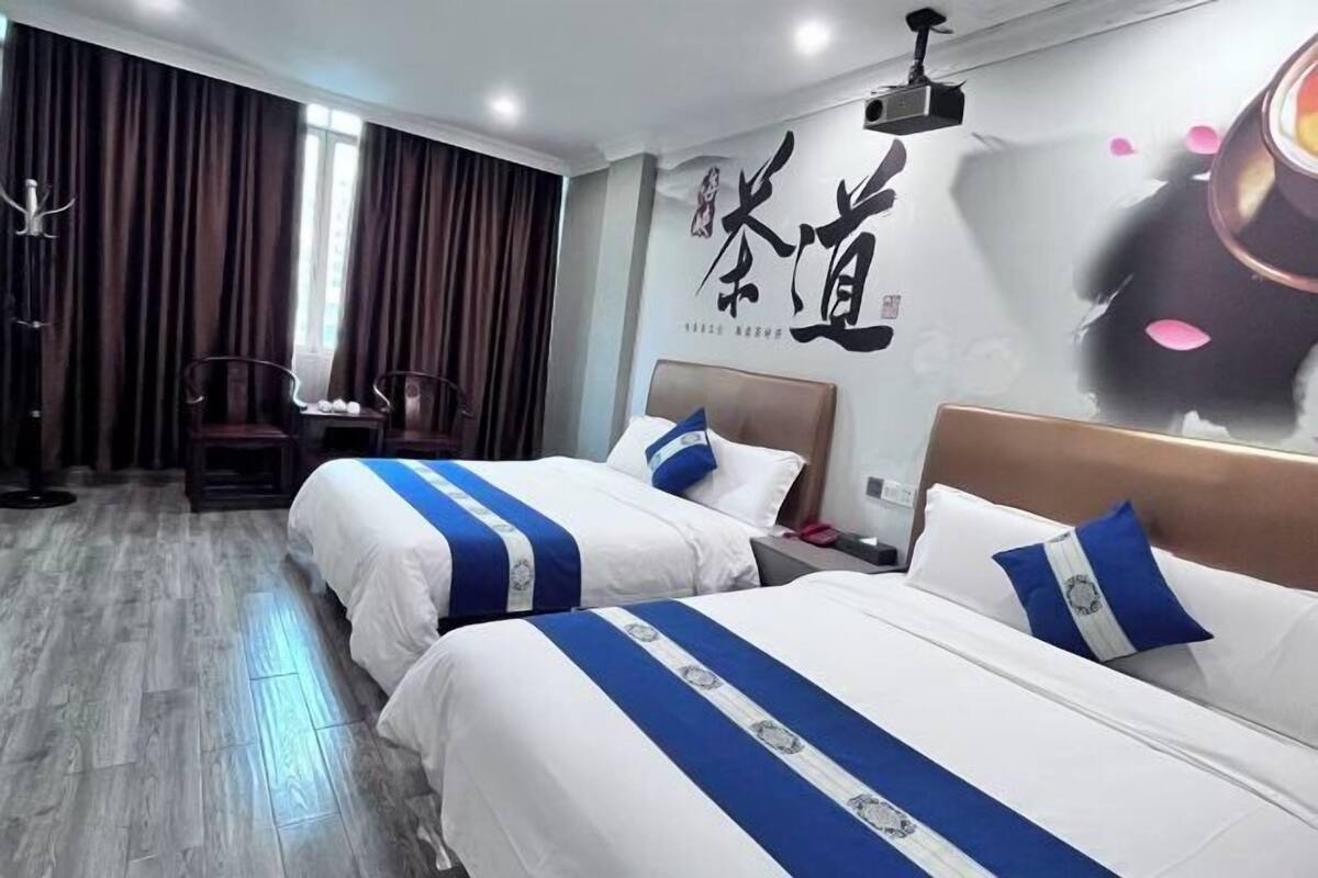 A hotel room with two beds, a desk, and a chair. There is a large wall with Chinese characters and a painting.