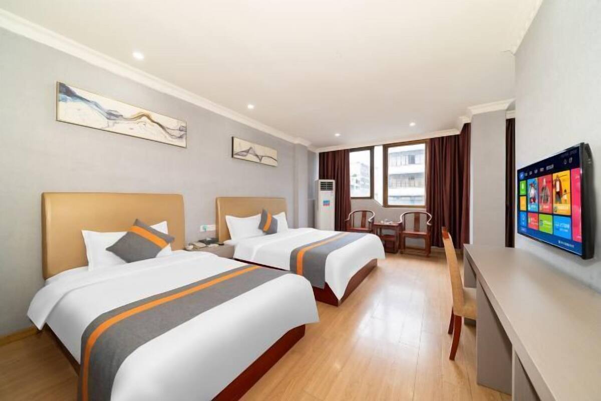 A hotel room with two beds, a desk, a TV, and artwork on the walls.