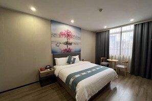 A hotel room with a bed, a nightstand, a small table, and a chair. There is a painting on the wall above the bed. - Yide Hotel (Yingde Pearl Plaza Pedestrian Street) (Yingde)