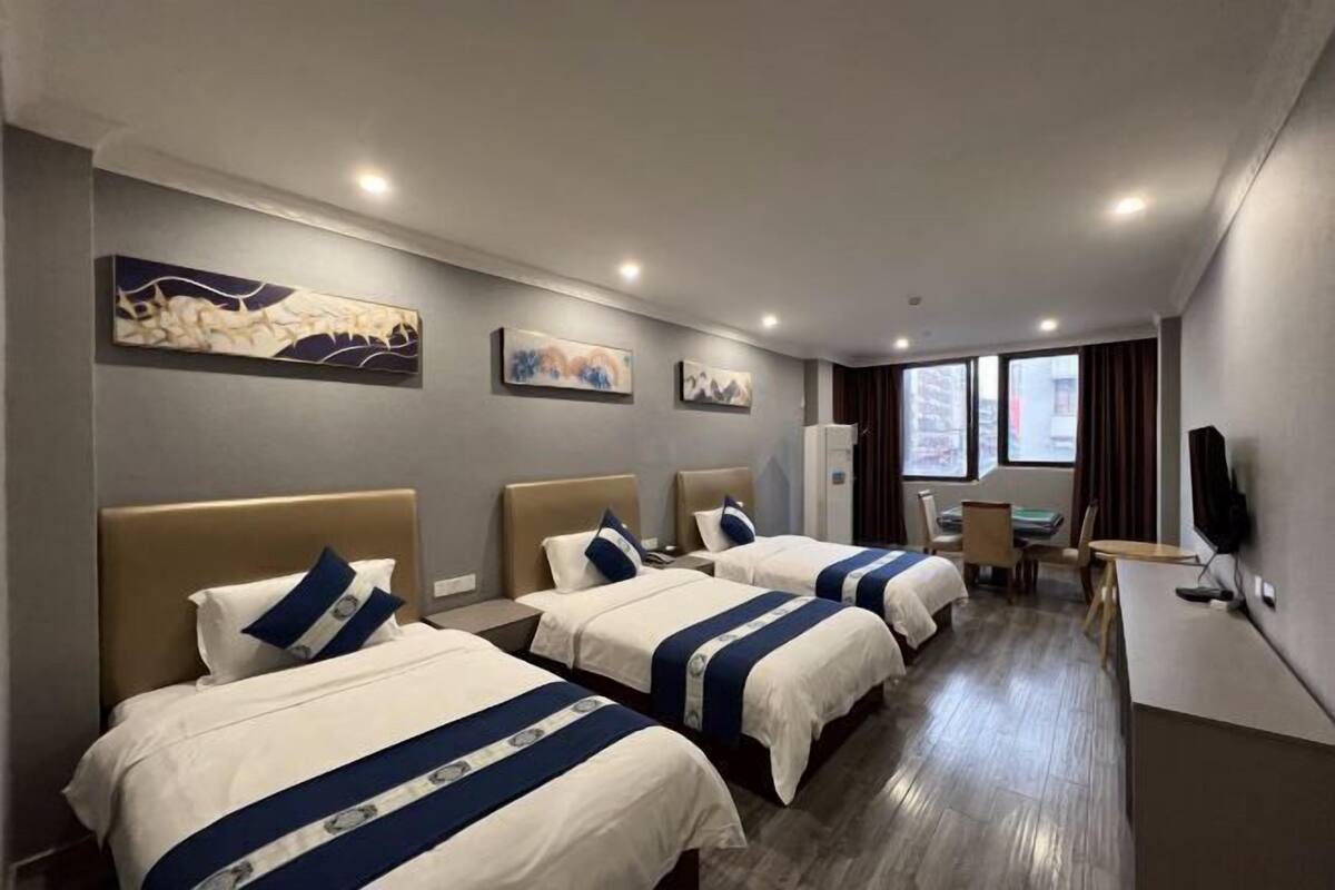 A hotel room with three beds, a desk, and a TV.