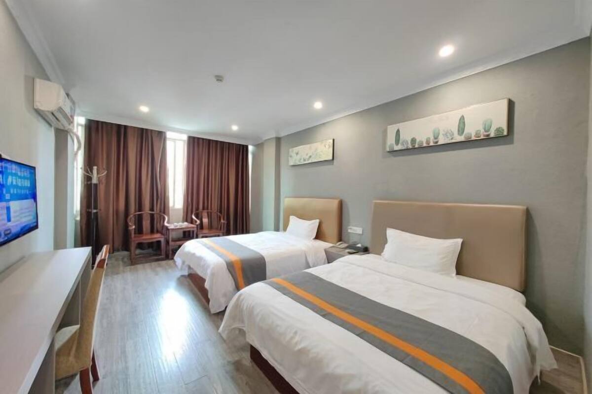 A hotel room with two beds, a desk, a chair, a television, and a window with curtains.