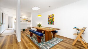 Eine moderne Küche mit weißen Schränken, einem Holzespeisetisch mit blauen Kissen und einem farbenfrohen Tulpenbild an der Wand.