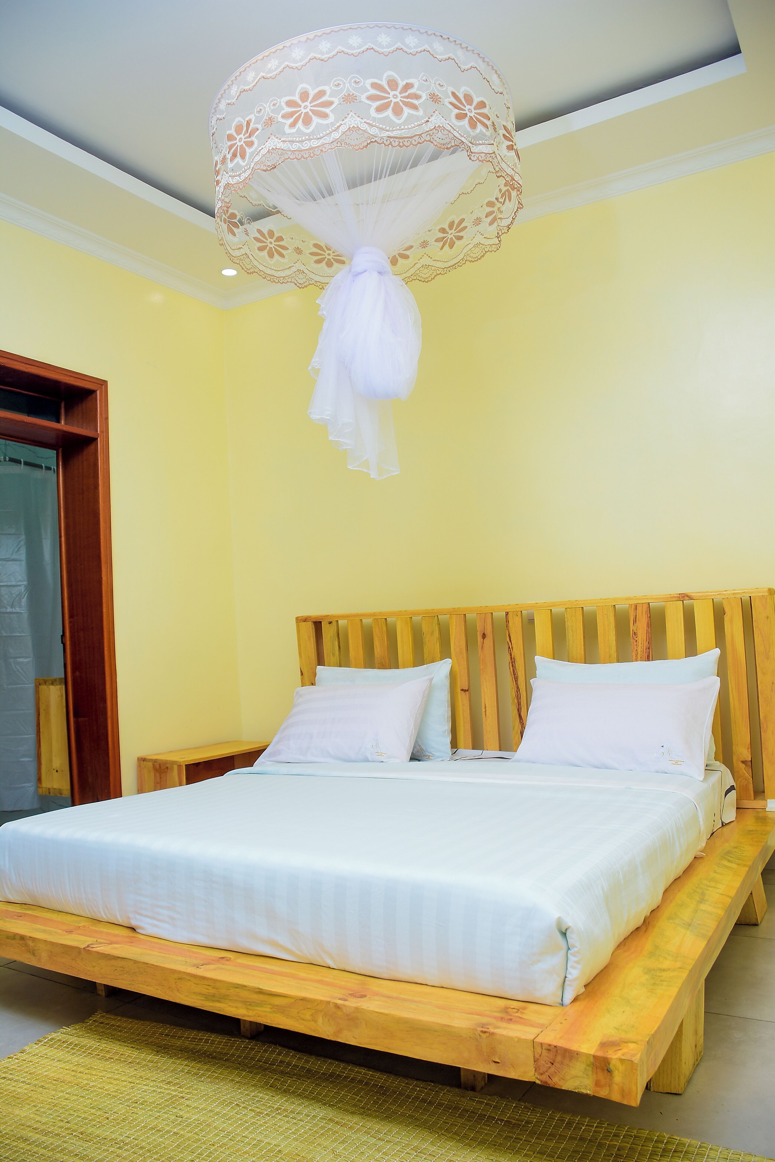 Una cama con cabecera de madera, ropa de cama blanca y un mosquitero sobre ella.