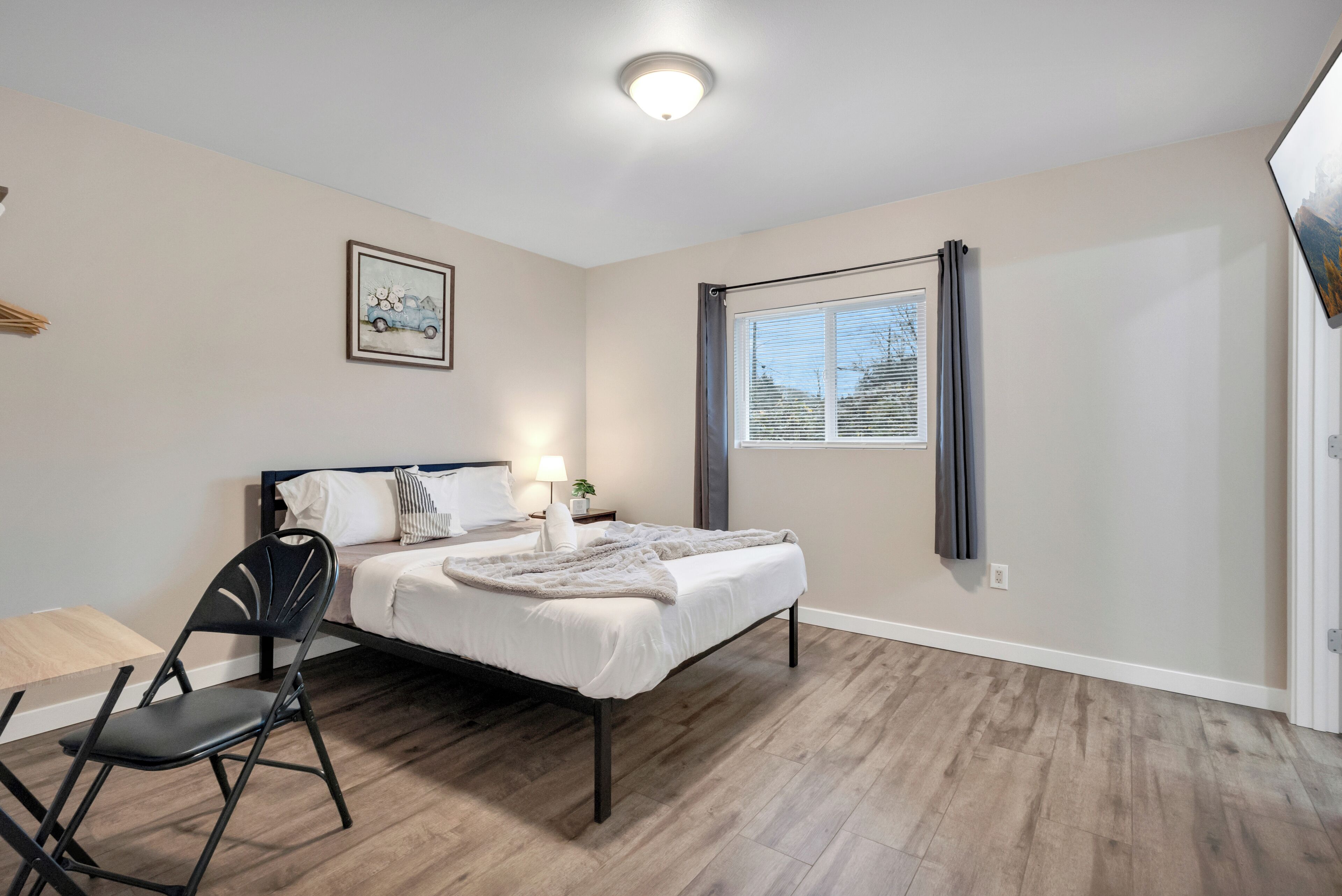 Une chambre à coucher avec un lit, une chaise, une fenêtre et un tableau accroché au mur.