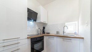 A modern kitchen with white cabinets, a black oven, a stainless steel sink, and a window providing natural light. - The Sweet yachtsman (Mulhouse)