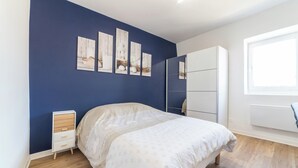 A bedroom with a bed, a nightstand, a wardrobe, and artwork on the wall. - The Sweet yachtsman (Mulhouse)