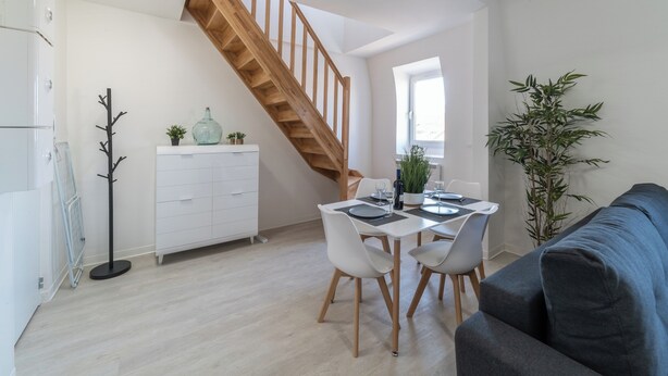 Een moderne keuken met witte kasten, een houten trap, een eetgedeelte met witte stoelen en een grote potplant.