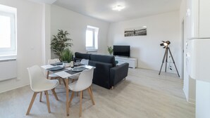 Een moderne woonkamer met een bank, een eettafel met stoelen, een televisie, een statief en een potplant.