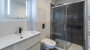 Een moderne badkamer met een wit wastafelmeubel, toilet en een douchecabine.