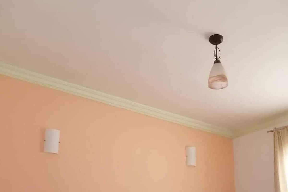 A room with two beds, peach-colored walls, and a single hanging light fixture.
