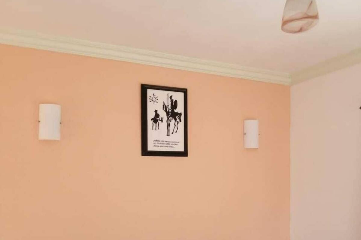 A bedroom with a bed, a framed picture on the wall, and a ceiling light.
