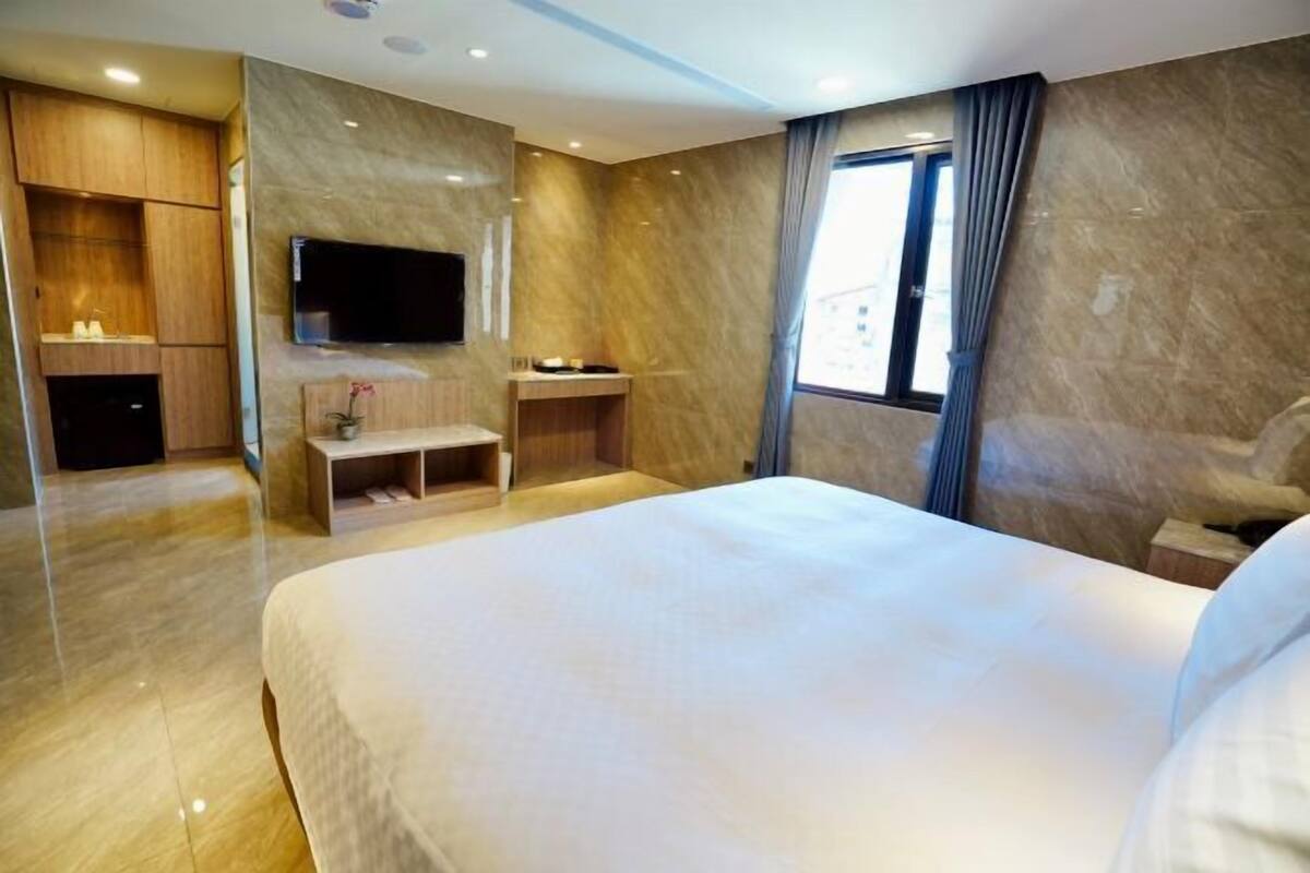 Camera d'albergo moderna con un letto grande, una TV a parete, un piccolo angolo salotto e una finestra con tende.