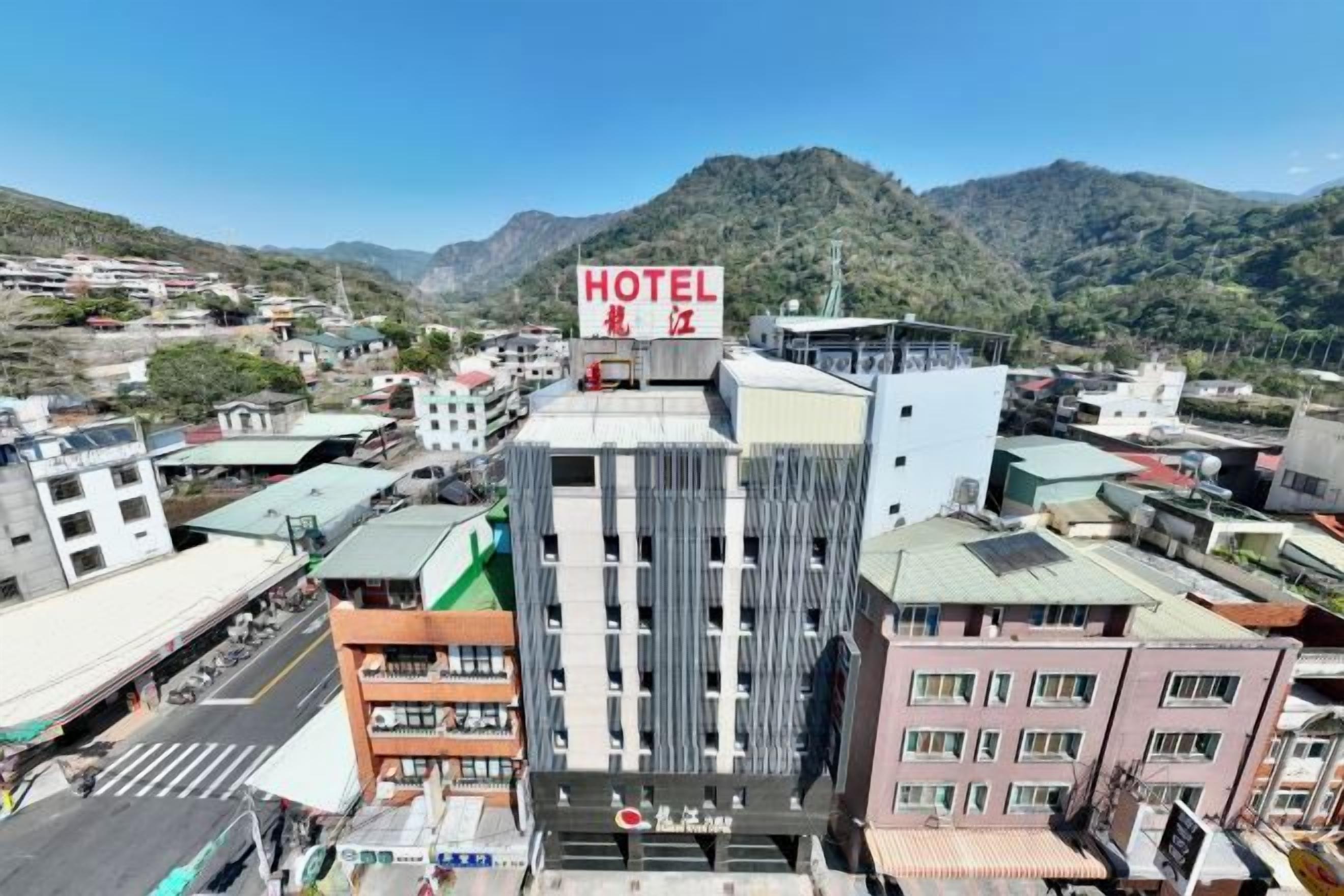 A hotel with a prominent sign, surrounded by buildings and a mountainous backdrop.