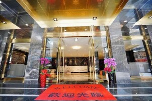 Entrada de hotel con mostrador de recepción de mármol, alfombra roja y dos arreglos florales.