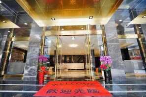Un hall d’hôtel avec un comptoir d’accueil, un tapis rouge et deux compositions florales.