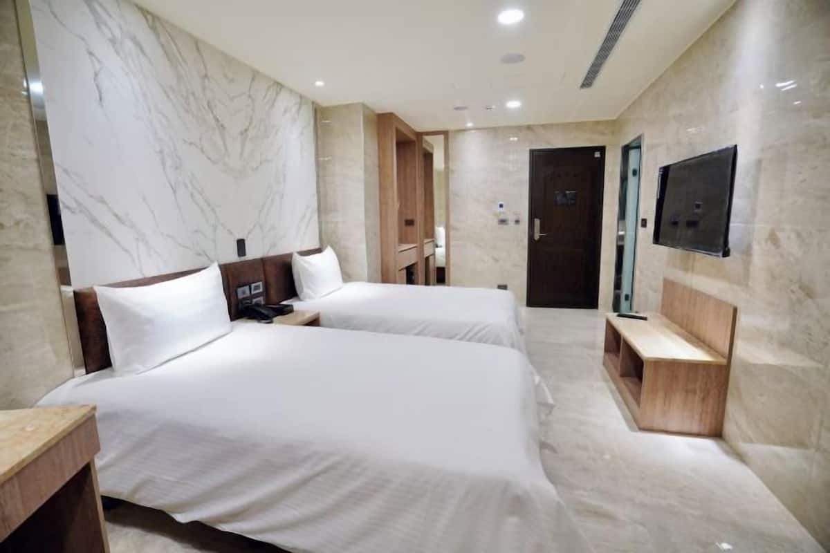 Camera d'hotel con due letti, televisore, una panca in legno e pareti in marmo.