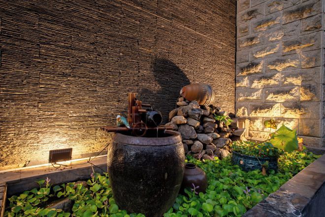 A stone wall with a water feature, including a large pot and a small fountain.