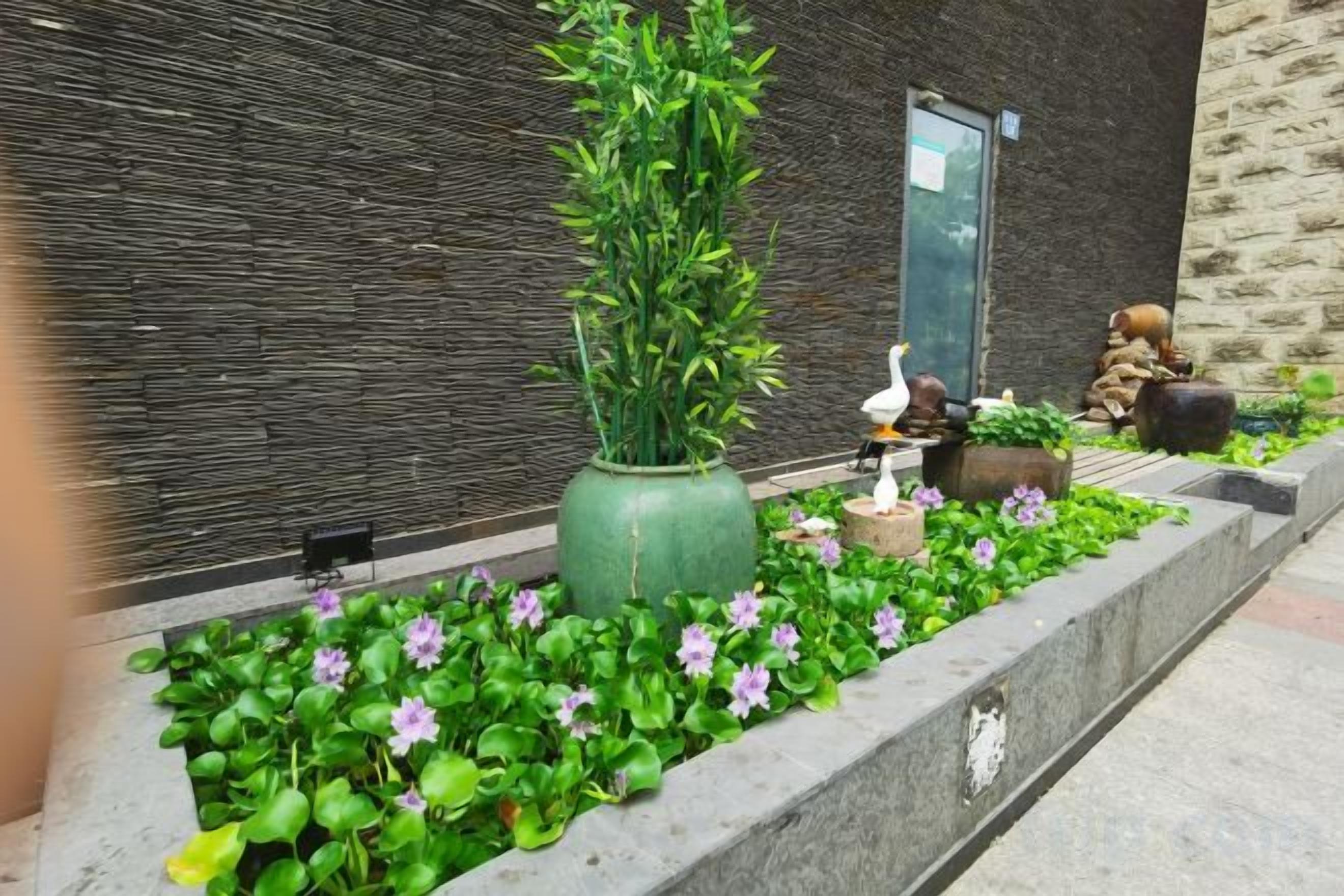 A landscaped garden area with a large green planter, a bird sculpture, and a small pond with a statue.