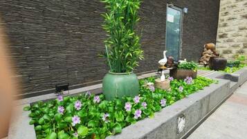 A landscaped garden area with a large green planter, a bird sculpture, and a small pond with a statue.
