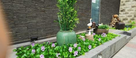 A landscaped garden area with a large green planter, a bird sculpture, and a small pond with a statue.