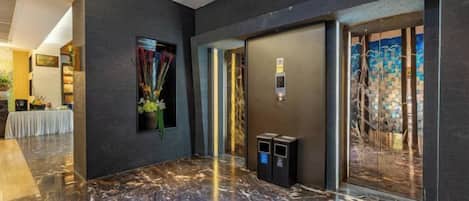 Un vestíbulo con piso de mármol, un mostrador de recepción y un panel de control de ascensor instalado en la pared.