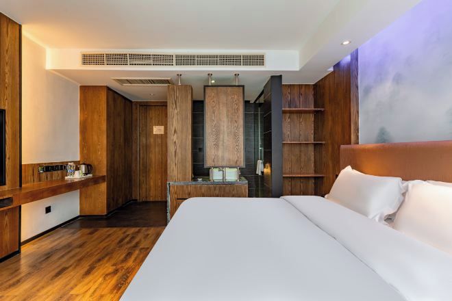 Habitación de hotel moderna con una cama grande, paneles de madera, un escritorio empotrado y una zona de estar con vista a la ciudad.