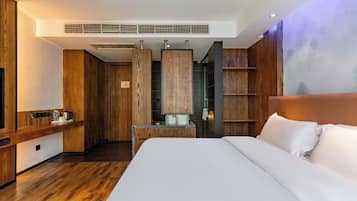 Habitación de hotel moderna con una cama grande, paneles de madera, un escritorio empotrado y una zona de estar con vista a la ciudad.