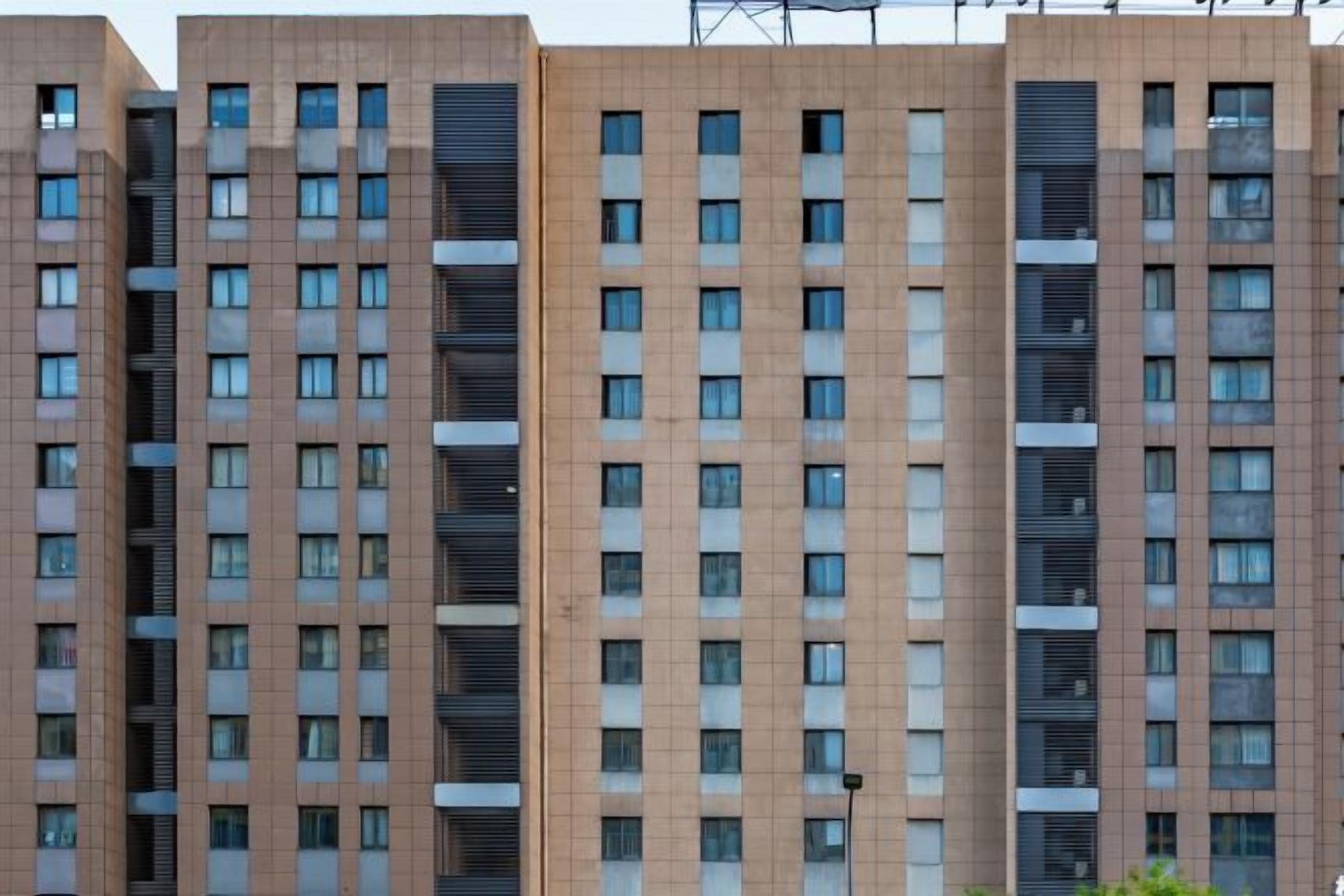 Un edificio residencial de varios pisos con fachada uniforme, numerosas ventanas y una unidad central de aire acondicionado.