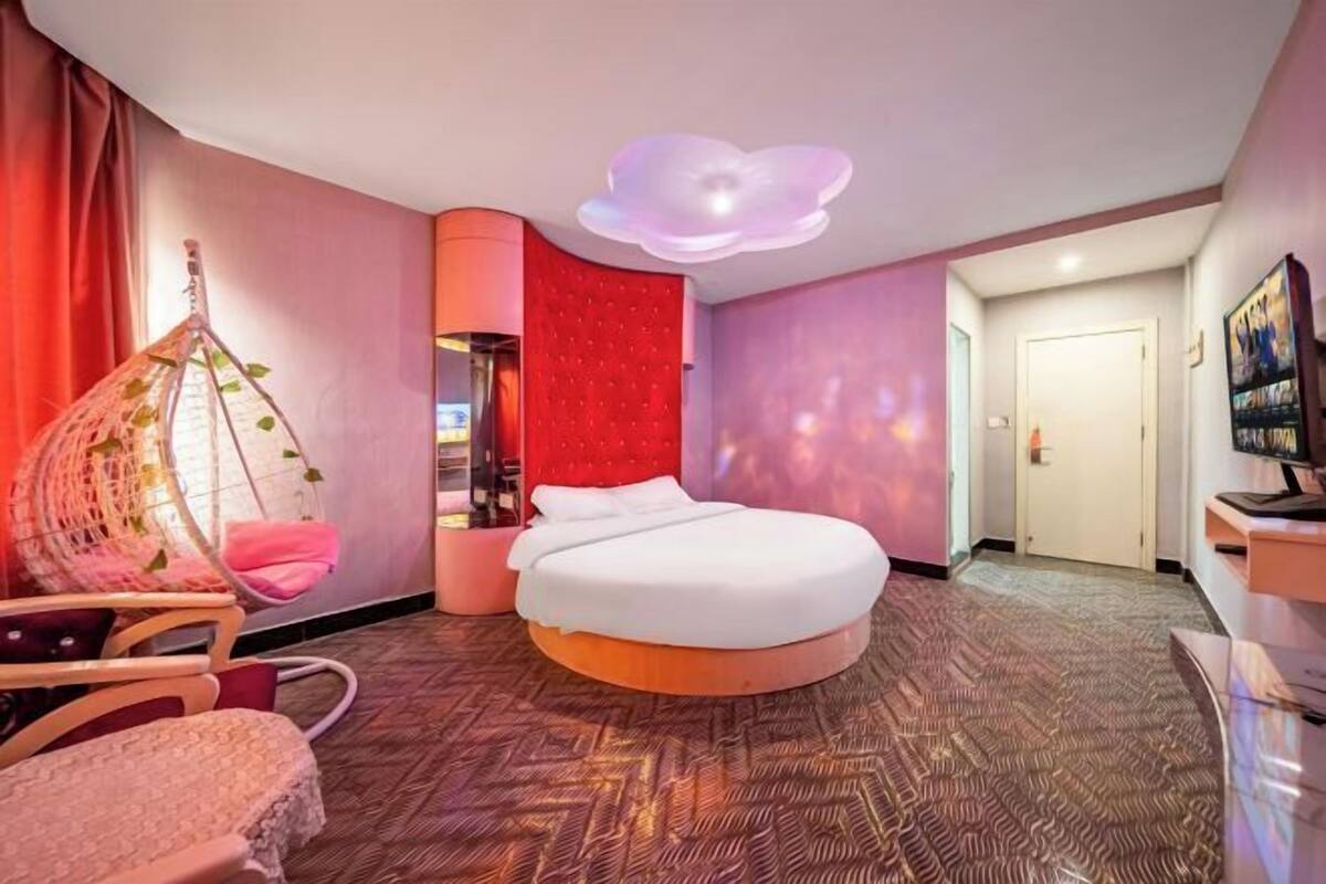 A modern hotel room with a round bed, a hanging chair, and a unique ceiling light fixture.