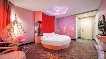 A modern hotel room with a round bed, a hanging chair, and a unique ceiling light fixture.