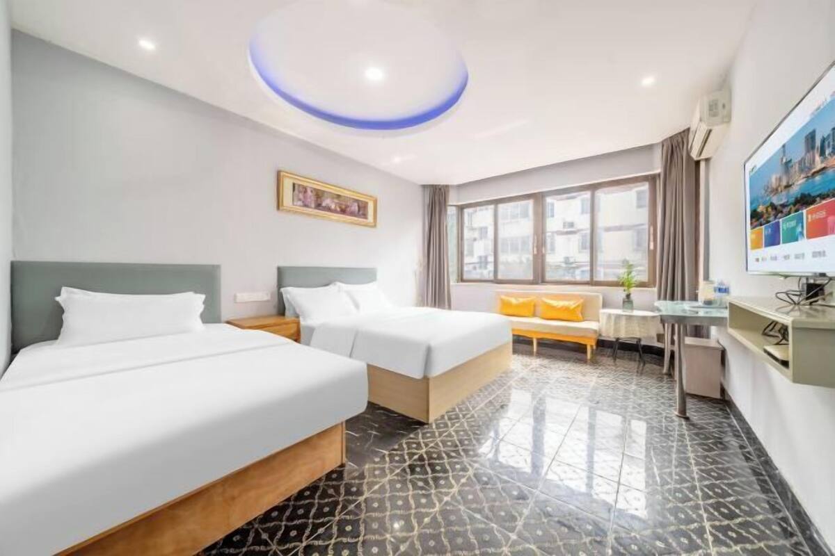 A hotel room with two beds, a sofa, a small table, a TV, and a window with curtains.