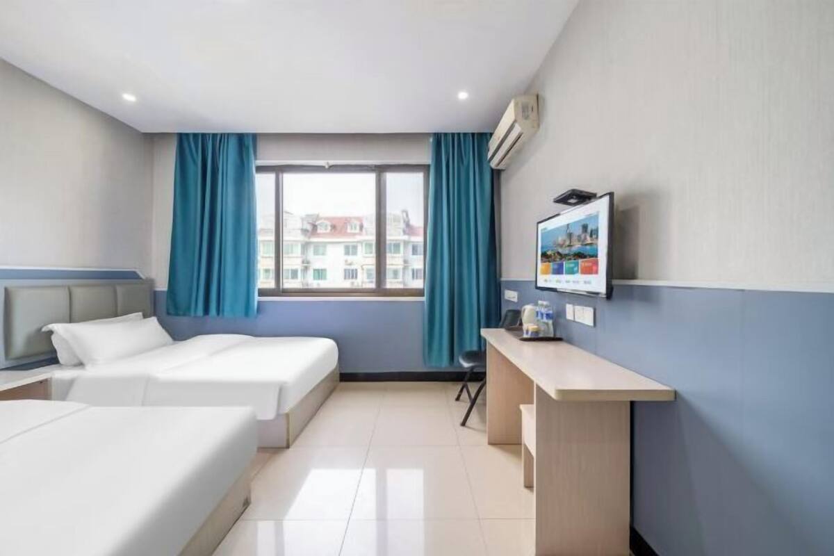 A hotel room with two beds, a desk, a TV, and a window with curtains.