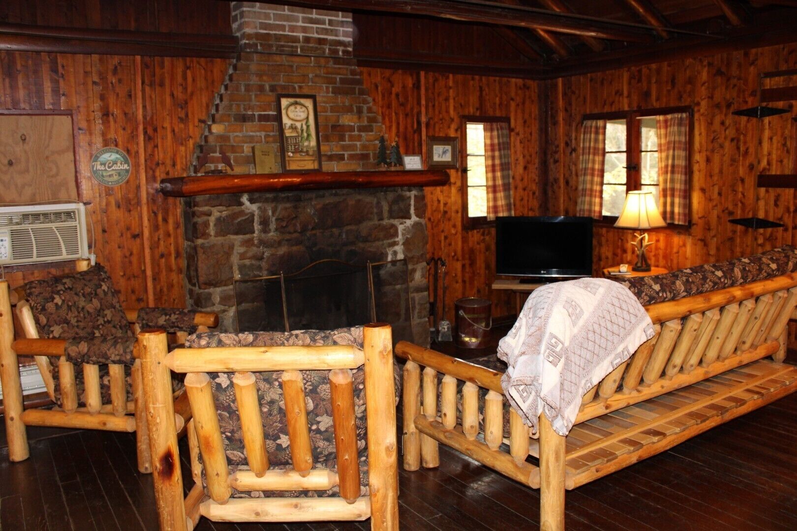 Un interior de cabaña acogedor con chimenea de piedra, mobiliario de madera y un televisor.
