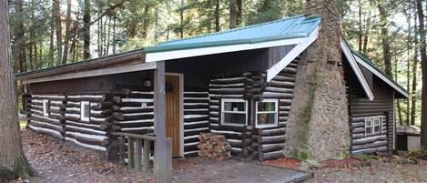 A rustic log cabin with a stone chimney, a covered porch, and a small window.